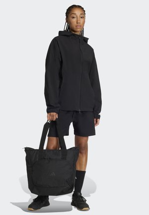 Zwarte waterdichte jas met rits, gecombineerd met zwarte korte broek en bijpassende tas. De tas heeft twee schouderbanden en een voorvak.