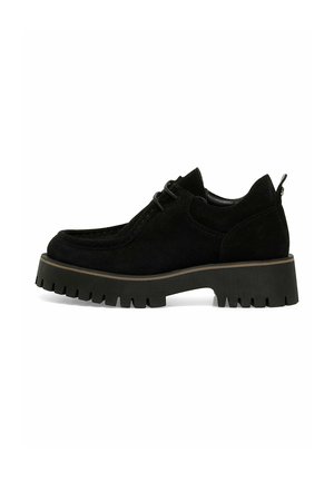 Scarpa in suede nero con design moccasin, punta rotonda e suola in gomma chunky caratterizzata da un battistrada spesso. Include dettagli cuciti e chiusura con lacci.