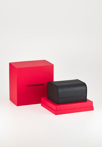 Fekete, texturált bőrdoboz lekerekített tetejével, két piros dobozra helyezve. A nagyobb piros dobozon a "FERRAGAMO" felirat fekete betűkkel olvasható.