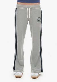Szare spodnie dresowe z granatowymi paskami po bokach, z regulacją w pasie na sznurek oraz logo "Superdry Athletic". Rozszerzający się krój, miękka tkanina oraz prążkowana tekstura w pasie.