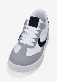 Sneaker bianco con accenti in suede grigio, dettagli neri, punta testurizzata e lacci bianchi. Include un colletto imbottito e suola in gomma.