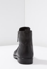 Botín de cuero negro hasta el tobillo con cremallera lateral, textura suave, punta redondeada y detalle de costura mínima sobre una suela plana de goma.