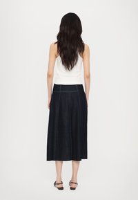 Mørk denimskjørt med grønn søm, A-linjeform, midt på leggen lengde, rå kant, kombinert med en tettsittende hvit tank topp og svarte sandaler.