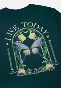 Donkergroen langemouwen shirt met een vlinder- en bloemgrafiek. De tekst luidt "LEEF VANDAAG" met decoratieve elementen en een logo.