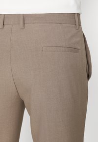 Bruna skräddarsydda byxor med en slät yta, flat bakficka och subtila sömnadsdetaljer. Lämpliga för avslappnad eller formell användning.