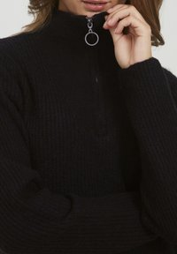 Maglione nero a coste con colletto alto e chiusura con zip corta, dotato di anello in argento per la trazione. Texture morbida e vestibilità rilassata.