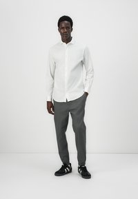 White long-sleeve button-up shirt paired with gray tapered pants and black sneakers. The outfit features a minimalist design and a smooth texture.
