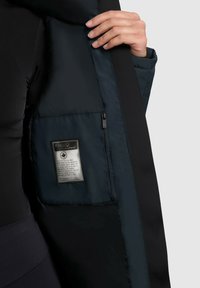 Interior de chaqueta acolchada azul oscuro con un bolsillo con cremallera y etiqueta de cuidado. Textura suave con elementos de diseño elegantes.