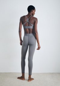 Šedá sportovní souprava zahrnující sportovní podprsenku s křížovým zadním dílem a legíny s vysokým pasem, obě vyrobené z hladkého, elastického materiálu.