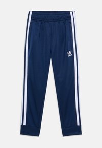 Marinblåa träningbyxor med vita sidostråk, elastisk midja och ribbade muddarna. Har Adidas-logotypen på vänster lår. Tillverkad av polyester.