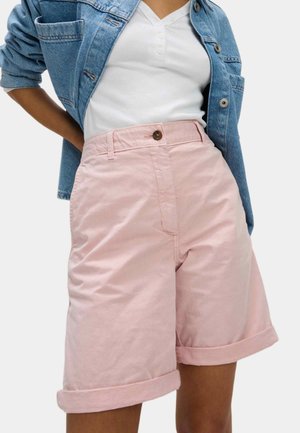 Kvinde iført lyserøde shorts med opfoldede ben, hvid ribbet henley-shirt og blå denimjakke med opskubbede ærmer.