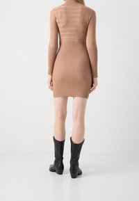 Robe moulante à côtes de couleur marron clair avec des manches longues et un col haut, accompagnée de bottes de cowboy noires ornées de broderies.