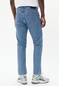 Jean en denim bleu clair avec une coupe droite, comportant deux poches arrière et une taille standard, associé à des baskets grises et bleues.