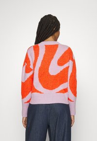 Pull en maille avec un motif tourbillonnant abstrait en orange et lavande, doté d'un ourlet et de poignets côtelés, et d'une coupe décontractée.