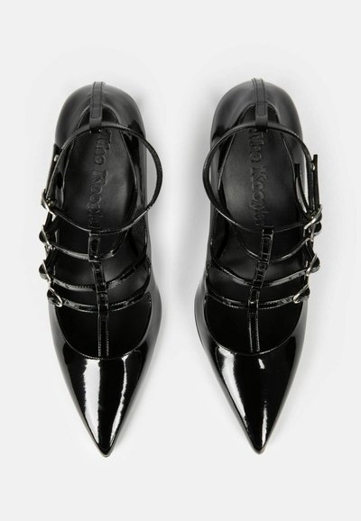 Ballerines en cuir verni noir à bout pointu avec bride en T et trois boucles latérales, vues de dessus sur fond blanc.