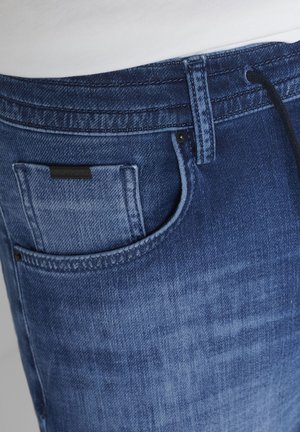 Primer plano de jeans de mezclilla azul con bolsillo delantero, pasador para cinturón y detalles sutiles de desgaste.