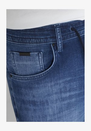 Nahaufnahme von blauen Jeans mit Vordertasche, Gürtelschlaufe und dezenten Verblassungen.