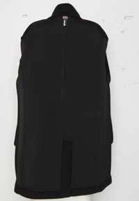 Manteau noir avec un col haut, un matériau extérieur lisse et une section inférieure texturée. Comprend une étiquette à l'arrière et des fentes sur les côtés pour une meilleure mobilité.