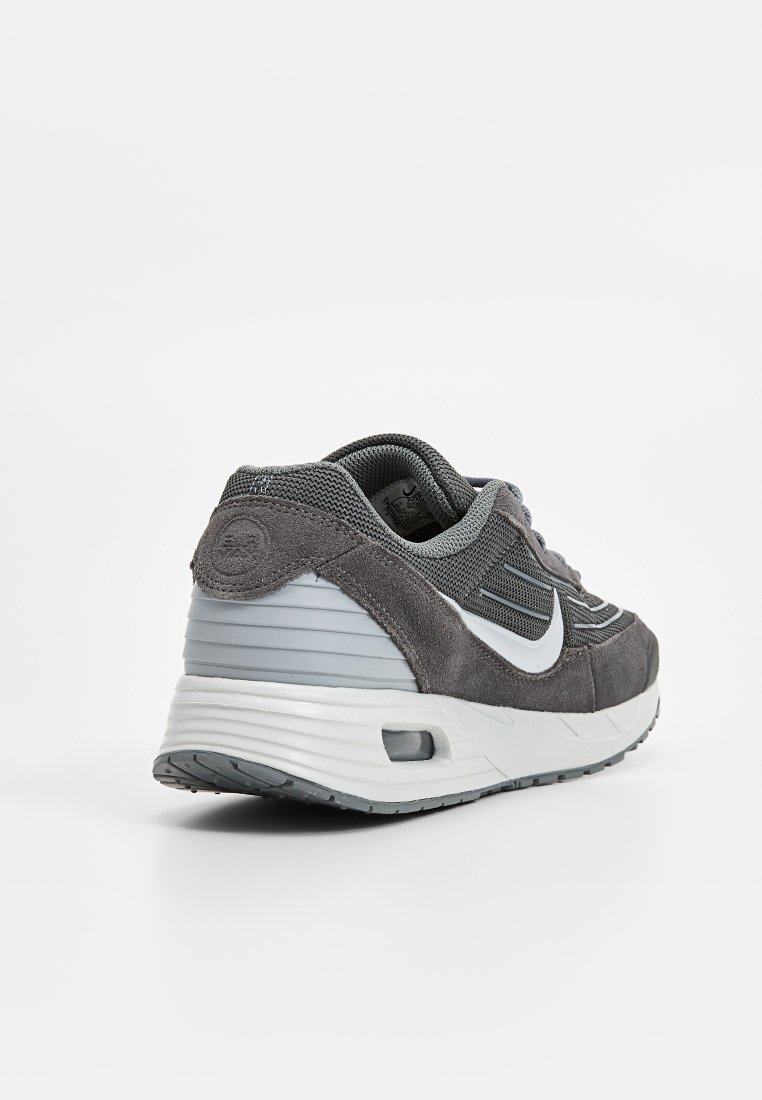 Chaussure de sport grise avec un dessus en suède texturé et en mesh, un swoosh Nike blanc distinct et une semelle rembourrée avec une unité d'air visible.
