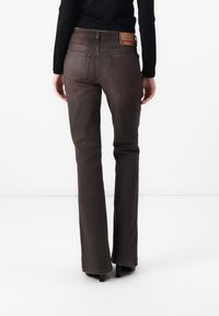 Brązowe dzwony dżinsowe, średnia faktura denimu, z dwoma tylnymi kieszeniami, kontrastującymi szwami oraz markową skórzaną naszywką na talii.