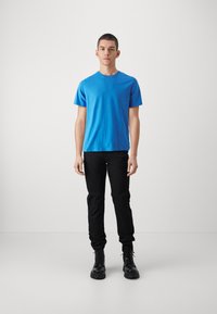 Kék pamut póló rövid ujjakkal, fekete slim-fit nadrággal és fekete fűzős csizmával, melynek texturált talpa van.
