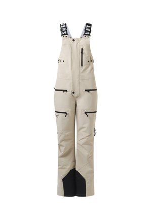 Pantalon à bavette beige avec jambes inférieures renforcées noires, plusieurs poches zippées et bretelles réglables noires et blanches avec logo.
