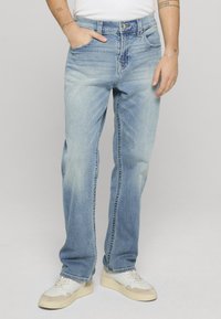 Vaqueros de mezclilla azul claro con un corte holgado, que cuentan con cinco bolsillos, cierre de cremallera y un desvanecimiento sutil. Combinados con zapatillas blancas.