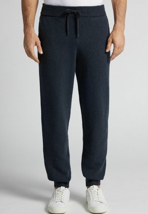 Marineblaue Sweatpants mit weichem Material, geripptem Bund und Kordelzug. Eng anliegenden Bündchen an den Knöcheln. Kombiniert mit weißen Sneakers.