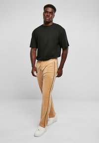 Zwarte korte mouwen t-shirt gecombineerd met lichtbruine velours broek met zwarte zijsrepen en witte sneakers.