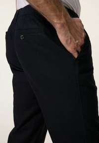 Tummansinisiä puuvillahousuja, joissa on sileä pinta. Housuissa on sivutaskut ja takana napillinen tasku. Vyötärö on rento istuvuus.