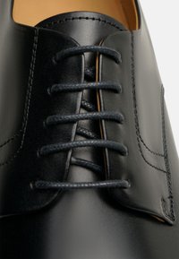 Chaussure habillée en cuir noir avec bout arrondi, accents cousus et un laçage classique avec des lacets noirs assortis.