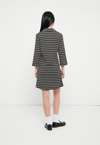 Pasiasta sukienka ma czarno-białym wzorze, rękawy do trzech czwarte, dopasowany pas i rozkloszowaną spódnicę, zestawiona z czarnymi butami i białymi skarpetkami.