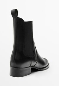 Bottine en cuir noir avec panneau élastique sur le côté, languette à l'arrière, talon bas empilé et bout arrondi, vue de côté arrière.