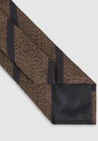 Pruun ja tumesinine triibuline lips tekstuuriga kudumiga. Lipsu otsas on stabiilsuse tagamiseks tahke tume kangatükk.