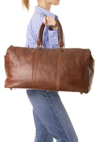 Borsa da viaggio in pelle marrone con superficie texturizzata, due manici robusti e piedi in metallo. Caratterizzata da cuciture a contrasto e un design spazioso.