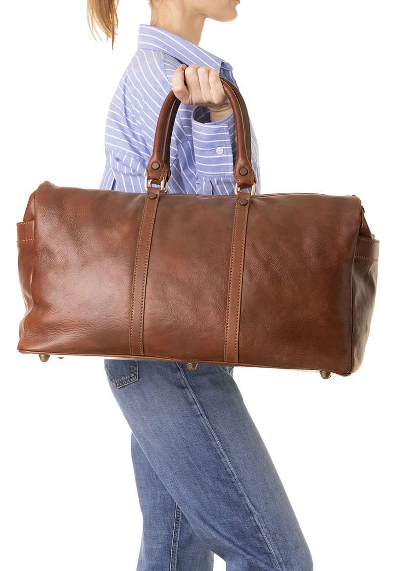 Borsa da viaggio in pelle marrone con superficie texturizzata, due manici robusti e piedi in metallo. Caratterizzata da cuciture a contrasto e un design spazioso.