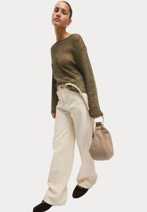 Pull en laine dans des tons de vert, pantalon large crème, tenant un sac beige avec une anse en anneau. Des chaussures brunes à enfiler complètent l'ensemble.