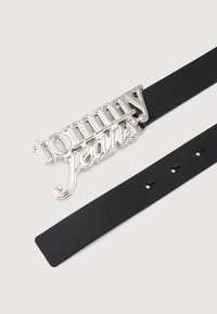 Μαύρη ζώνη με γυαλιστερή ασημένια πόρπη που φέρει το "tommy jeans" σε στυλιζαρισμένο γράμμα. Λείο υλικό με ρυθμιζόμενες τρύπες στη λωρίδα.