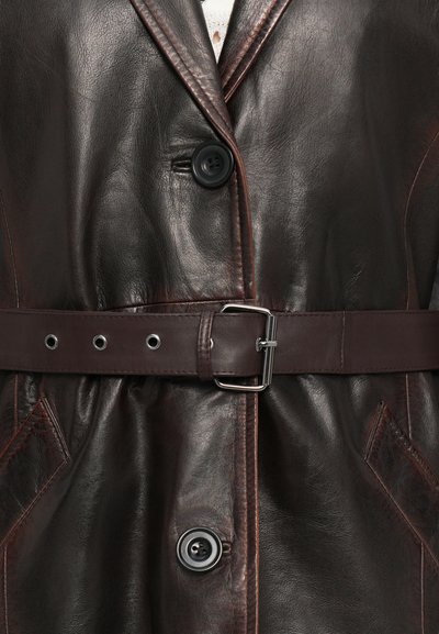 Cappotto in pelle marrone scuro con grandi bottoni neri, una cintura in pelle abbinata con fibbia in metallo e tasche frontali angolate.