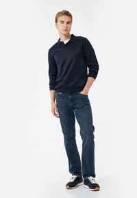 Polo de manga larga azul marino con cuello clásico, combinado con jeans de color azul oscuro y zapatillas negras con cordones crema y suelas texturizadas.