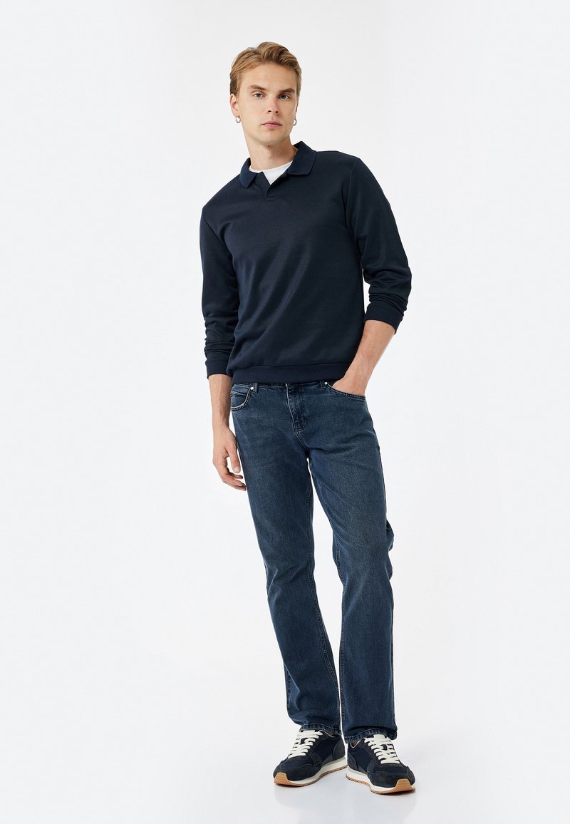 Polo de manga larga azul marino con cuello clásico, combinado con jeans de color azul oscuro y zapatillas negras con cordones crema y suelas texturizadas.