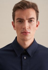 Polo blu navy con colletto classico, pattina anteriore e chiusura a due bottoni. Presenta una texture liscia e una vestibilità su misura.