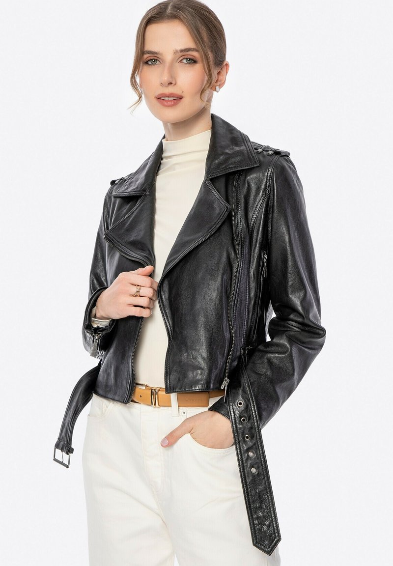 Schwarze Leder-Bikerjacke mit taillierten Design, Reißverschluss vorne, Reißverschlusstaschen an den Seiten und Knopfakzenten an den Ärmeln, kombiniert mit einem crèmefarbenen Oberteil.