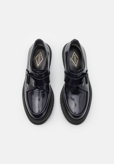 Pantofi din piele veritabilă lucioasă, negri, cu vârful rotunjit, având o curea lată pe instep și tălpi din cauciuc cu margini texturate. Branding auriu în interior.