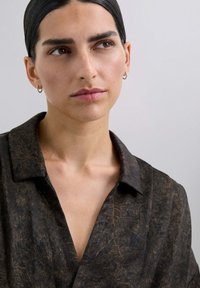 Camisa negra con una tela texturizada y estampada que presenta detalles dorados. Tiene un cuello, un diseño abotonado y un corte relajado.