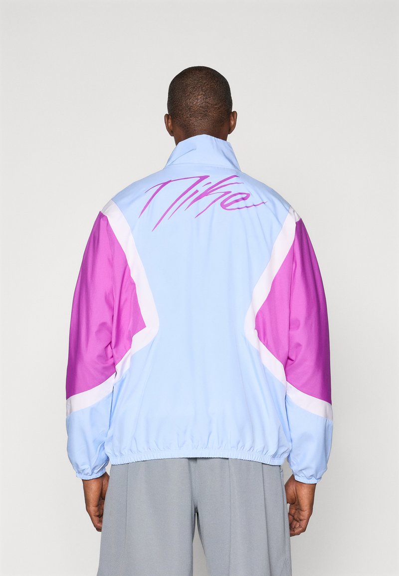 Light blue jacket with pink and white accents, featuring a high collar and elastic cuffs. Large "Nike" logo in pink on the back.