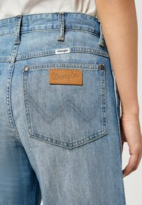 Ljusblå denimjeans har en läderpatch från Wrangler på bakfickan, med kontrasterande röd sömnad och ett zigzag-mönster.