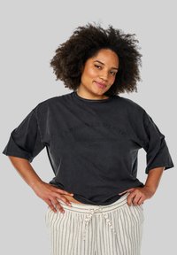 Sort oversized t-shirt med korte ærmer, der har et grafikprint i mørkegrå. Kombineret med cremefarvede stribede bukser med snøre.