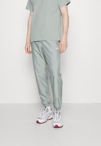 Ljusgröna, lätta, avsmalnande byxor med elastiska mudd, tillsammans med en matchande t-shirt och vita sneakers med röda accenter.