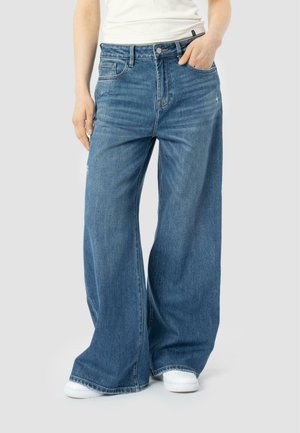 Wide-leg blue denim jeans with a high waist, slight fading, five pockets, and stitching details. Paired with white sneakers.